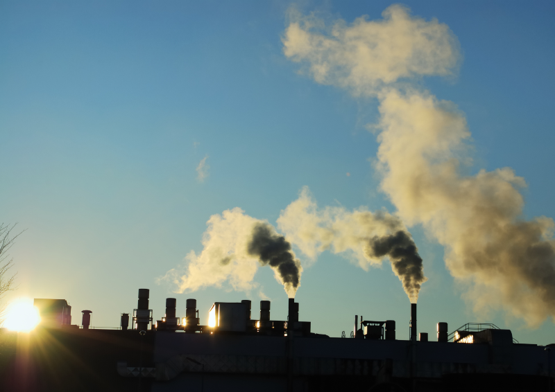 A row of industrial buildings release clouds of grey smoke into the air