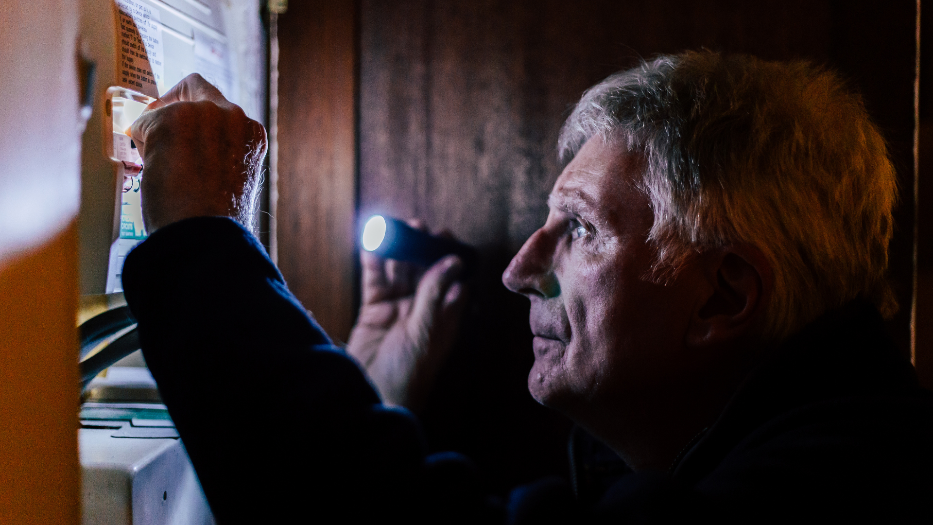 A man using a torch to examine a fuse box in the dark
